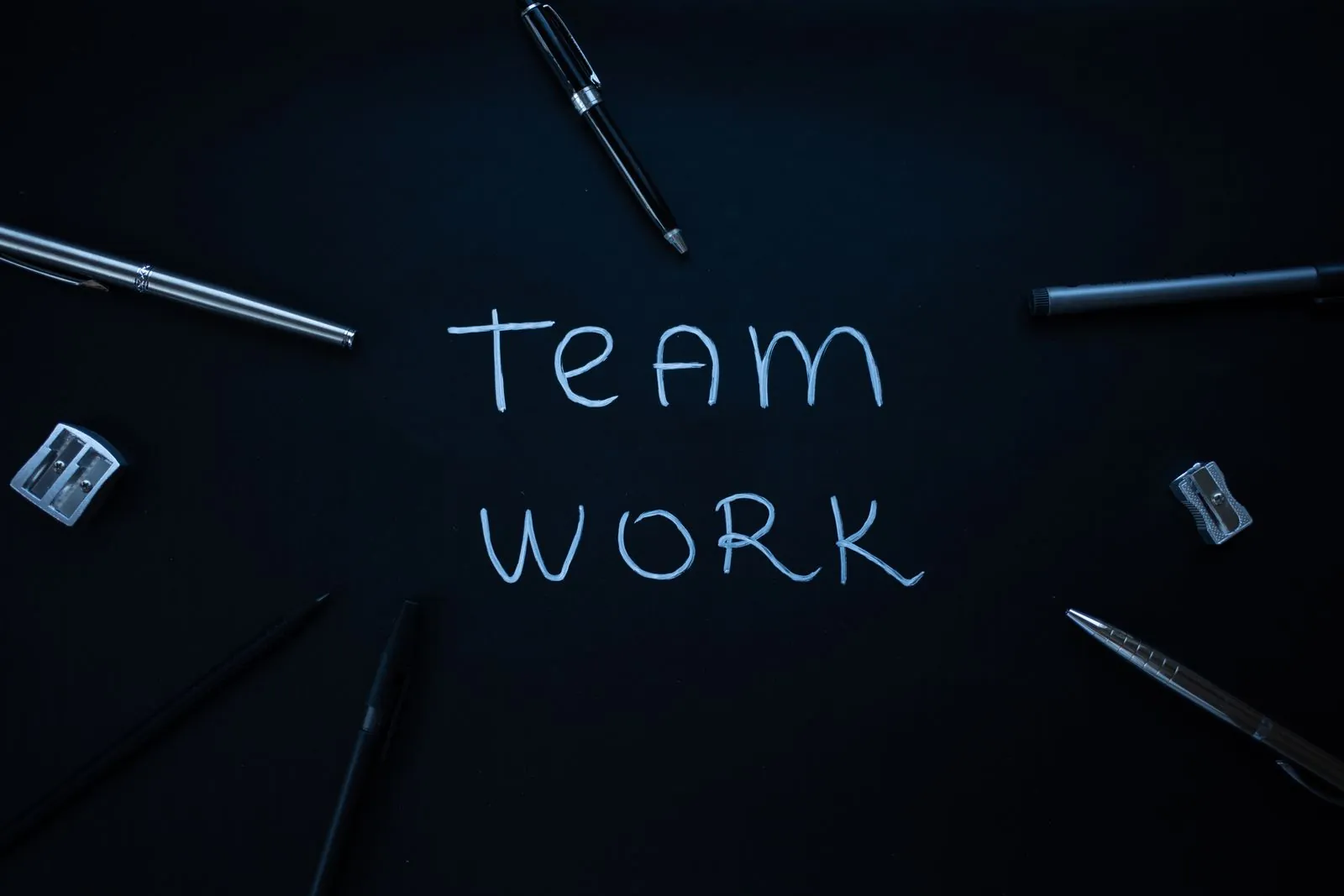 Ordet teamwork på sort baggrund omgivet af kuglepenne
